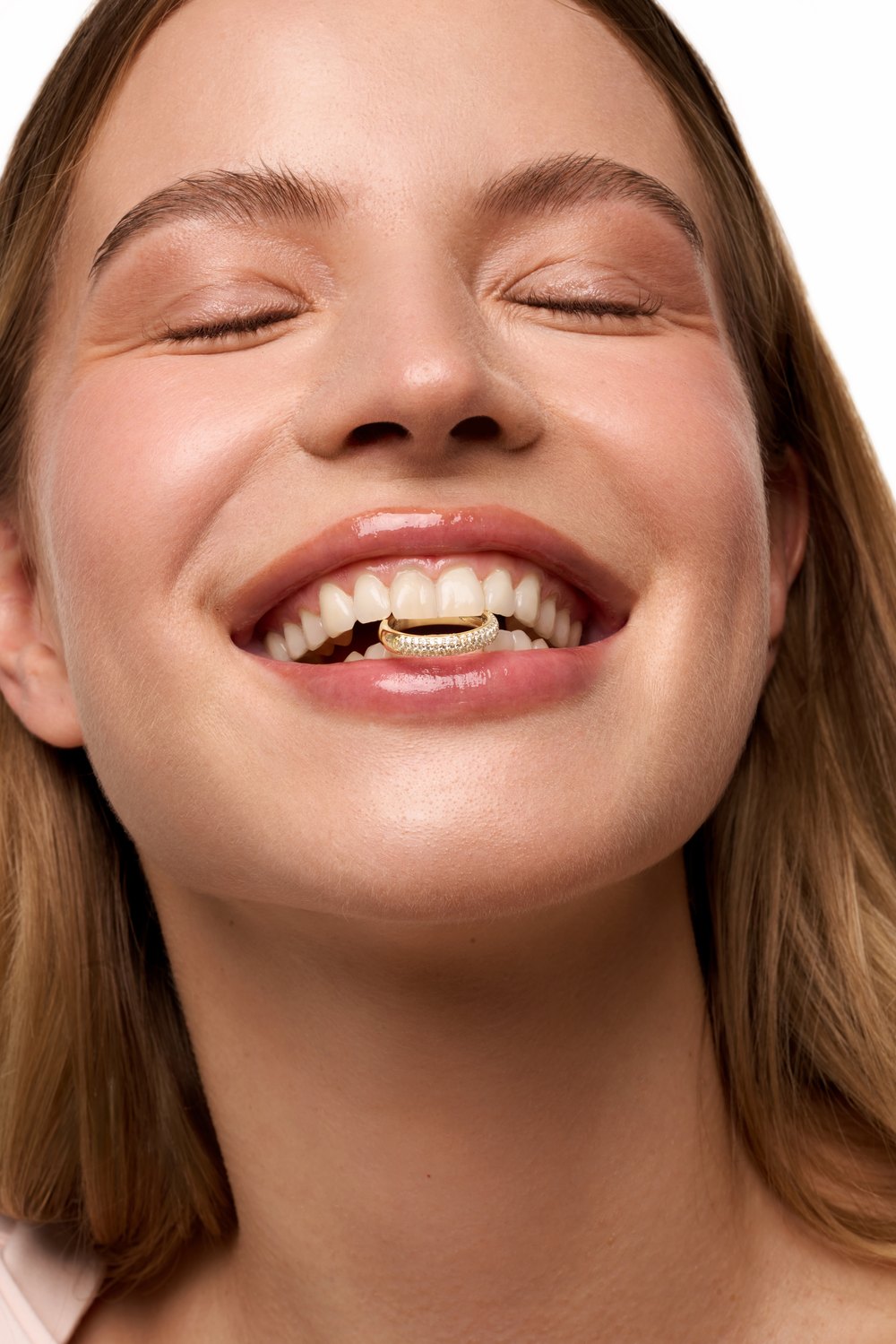 Smiling model holding a gold pavé ring between her teeth