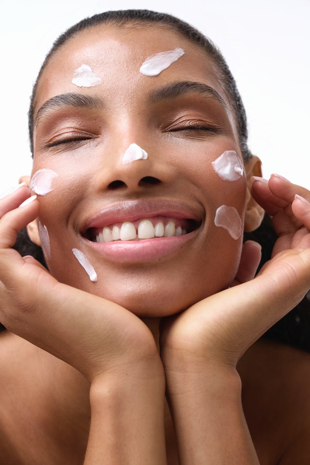 Smiling model with dabs of face cream on her skin
