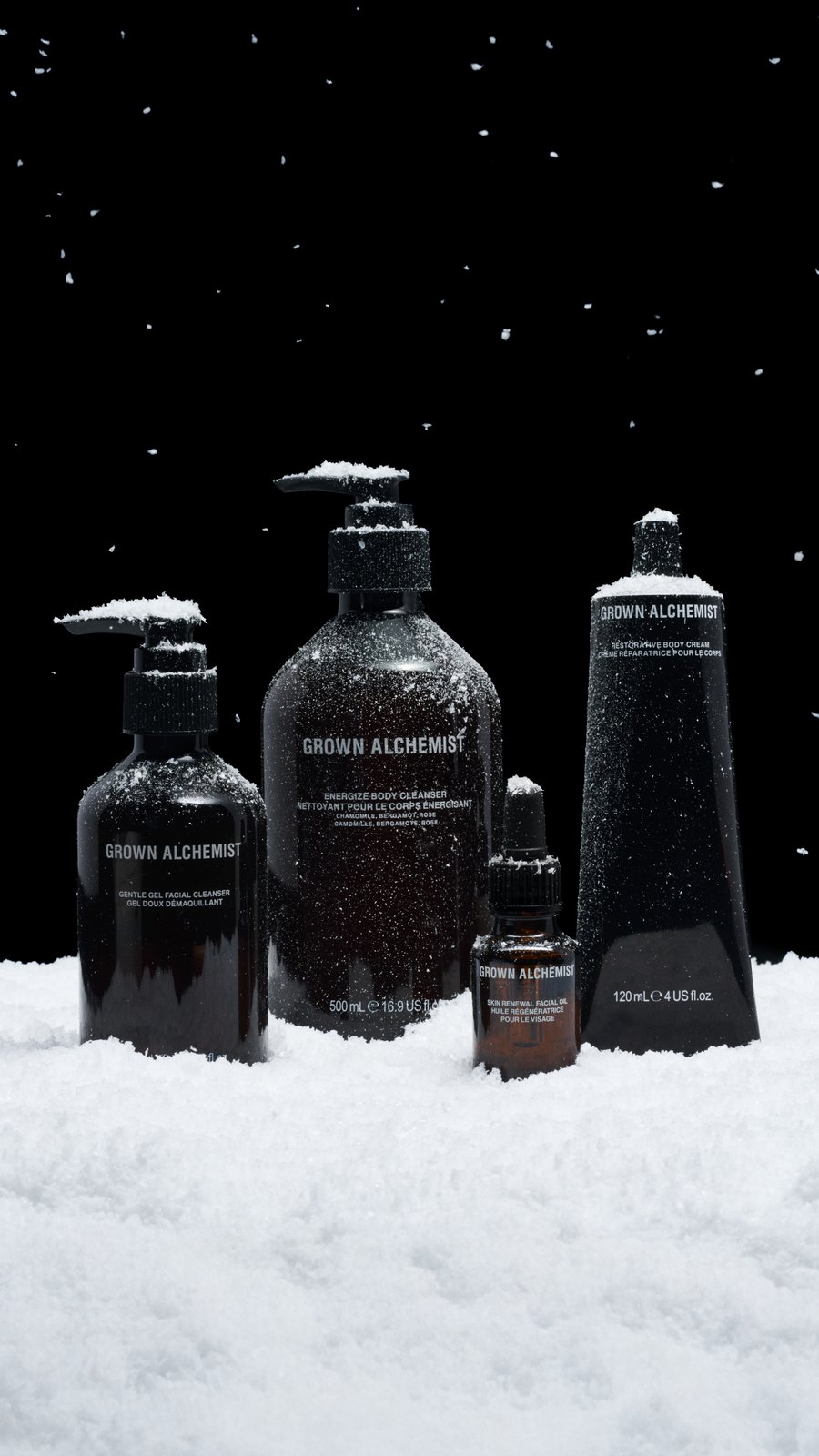 Grown Alchemist bottles dusted with snow against a black background