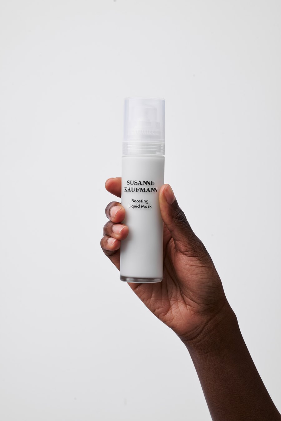 Hand holding a Susanne Kaufmann Boosting Liquid Mask bottle against a pale grey backdrop